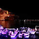 Una magica festa a Ischia: barche illuminate e gente festante con il castello illuminato sullo sfondo.