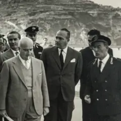 Angelo Rizzoli, con abito scuro, cammina con altri uomini a Ischia, sullo sfondo una collina terrazzata.