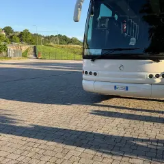 Un bus bianco attende su un parcheggio lastricato, pronto a percorrere le strade di Ischia. Un autista in divisa controlla il bagaglio.
