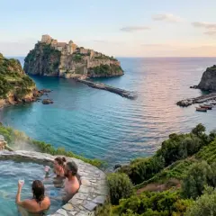 Coppie rilassate nelle terme naturali con vista sul castello e sul borgo di pescatori a Maronti, Ischia.