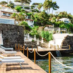 Terrazza in legno con lettini e ombrelloni, vista sul mare e sulle ville del **hotel i delfini Ischia** immerse nel verde.