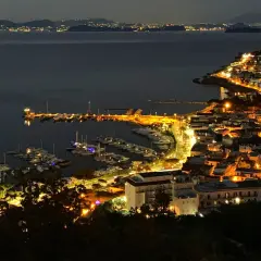 Casamicciola, un gioiello illuminato di notte, con un porto pieno di barche e luci che si riflettono sul mare calmo.