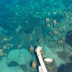 Acque cristalline e fondali rocciosi ad Aenaria, Ischia. Un pontile accoglie piccole imbarcazioni.
