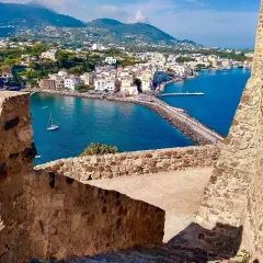Vista panoramica del porto di Ischia, con i traghetti in attesa e le case colorate che si affacciano sul mare blu.