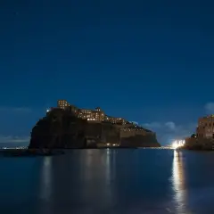Castello Aragonese illuminato di notte, riflesso sull'acqua, sotto un cielo stellato. Un'opera di Gabriele Mattera.