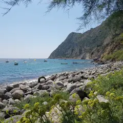La baia della Scarrupata, con le sue rocce levigate e il mare azzurro, accoglie piccole imbarcazioni. Un pontile si protende nell'acqua.