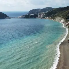 Vista aerea della spiaggia dei pescatori a Ischia, con case colorate aggrappate alla costa e un mare turchese.