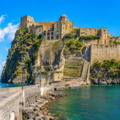 The Aragonese Castle on a rocky island, connected by a stone bridge, with boats in the turquoise sea.