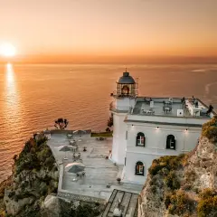 Hotel Faro Punta Imperatore a Ischia, con il sole che tramonta sul mare. Tavolini all'aperto e un bar sul tetto.