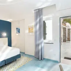 Camera luminosa con letto matrimoniale e vista su un cortile con ombrelloni blu. Un invito a soggiornare all'hotel oasi Ischia.