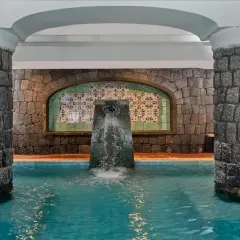 Piscina interna con fontana a cascata, colonne in pietra e piastrelle decorative. Un angolo di relax alle terme di Lacco Ameno.