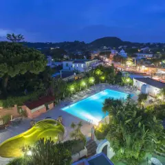 Piscina illuminata e vasca idromassaggio a forma di fagiolo al Hotel Eden Ischia, con vista sul paese di sera.