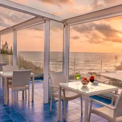 Terrazza con vista mare al tramonto, ideale per chi cerca dove alloggiare a Ischia senza macchina. Tavoli apparecchiati per aperitivo.
