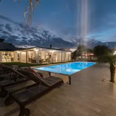 Piscina illuminata e lettini prendisole al tramonto, con cascata d'acqua. Un'oasi di relax al **hotel le palme Ischia**.