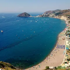 Vista aerea delle spiagge di Ischia, con ombrelloni colorati, mare blu intenso e tante barche all'orizzonte.