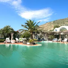 Piscina con palme e lettini, un angolo di paradiso tropicale a Ischia, con persone che si rilassano nell'acqua cristallina.