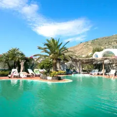 Piscina con lettini e palme, un'oasi di relax alle terme Sant'Angelo Ischia, con vista sulla collina verdeggiante.