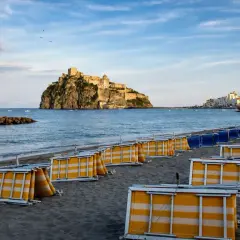 Spiaggia della Mandra a Ischia, con lettini piegati e il Castello Aragonese sullo sfondo.