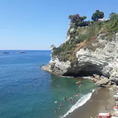 Scogliera bianca a picco sul mare turchese, con bagnanti e yacht all'orizzonte. La **cava grado Ischia** offre un rifugio naturale.