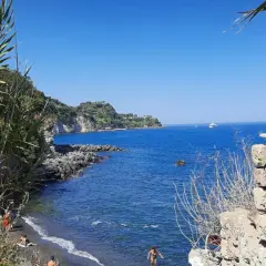 Spiaggia nera con gente che si gode il sole, scogli e il blu intenso del mare degli inglesi.