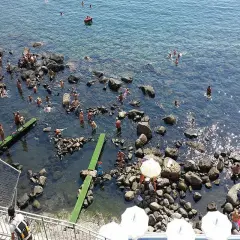 Persone si godono il sole e l'acqua cristallina nelle piscine naturali di Ischia, tra scogli e fondali trasparenti.