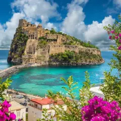 Castello Aragonese su uno scoglio, con mare turchese e fiori viola in primo piano. Una vittoria colonna di bellezza naturale.