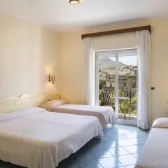 Camera con tre letti singoli, vista su un borgo di Alexander Ischia. Balcone con tavolo e sedie.