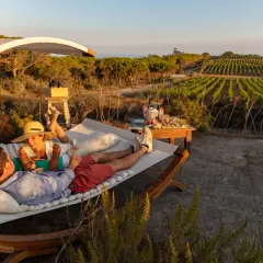 Coppia rilassata su un'amaca con vista su vigneti e mare, sorseggiando vino. Un perfetto sorgeto Ischia aperitivo al tramonto.