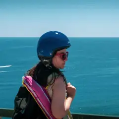 Ragazza con casco blu e zaino, guarda il mare. Pensa a come arrivare ad Ischia in auto, magari con uno scooter.