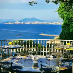 Tavoli apparecchiati con vista mare, un invito a cenare in uno dei ristoranti di Casamicciola. Il Vesuvio sullo sfondo.