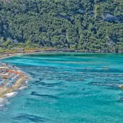 La spiaggia di Citara, con le sue acque cristalline e la rigogliosa vegetazione alle spalle, accoglie bagnanti e ombrelloni colorati.