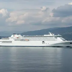 Traghetti per Ischia da dove partono? Questo grande traghetto bianco naviga in mare aperto, con montagne verdi sullo sfondo.