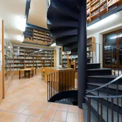 Interno della biblioteca antoniana ischia con scaffali pieni di libri, tavoli e una scala a chiocciola nera.