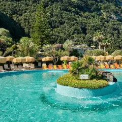 Piscina con lettini e ombrelloni a Ischia, immersa nel verde rigoglioso. Un'oasi di relax che ricorda la forza del **Tifeo** che dorme sotto l'isola.