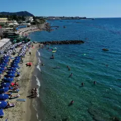 Forio Ischia spiagge affollate sotto il sole. Ombrelloni blu, bagnanti in mare e hotel affacciati sulla costa.