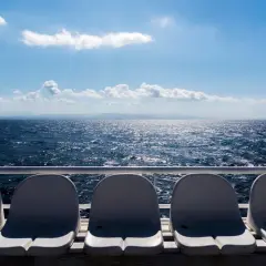 Sedili vuoti su un traghetto, con il mare blu scintillante e le montagne all'orizzonte. La differenza tra aliscafo e traghetto è evidente nella velocità e nel comfort.