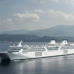 Un grande traghetto bianco solca il mare, pronto a portare passeggeri verso Ischia, con montagne verdi sullo sfondo.