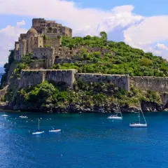 Ischia Ponte, con il maestoso Castello Aragonese che domina l'isola verdeggiante, circondato da un mare blu intenso e barche a vela.