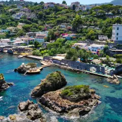 Baia di Cartaromana con rocce e acque cristalline. Case arroccate sulla collina. Scopri come arrivare a questa incantevole spiaggia.