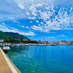 Porto di Forio, Ischia: barche a vela ormeggiate in un mare azzurro sotto un cielo con nuvole bianche. Per raggiungere Forio da Ischia Porto, si può prendere un autobus o un taxi.