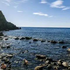 Persone e un cane si godono le acque calde della **baia di Sorgeto**, tra scogli e rocce a picco sul mare blu.