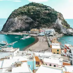 Baia con barche e case colorate a Ischia, con la rocca verde che domina il mare. Le cantine di Ischia offrono un panorama mozzafiato.