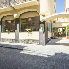 Ingresso elegante del **hotel Bristol Ischia**, con ampie vetrate, piante verdi e un'insegna storica.