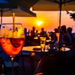 Un aperitivo rinfrescante con vista sul tramonto a Ischia centro sera. Persone sedute ai tavoli, ombrelloni e il sole che cala all'orizzonte.