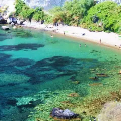 Acque cristalline e sabbia dorata nella spiaggia delle monache, incastonata tra scogliere rocciose e vegetazione rigogliosa.