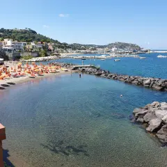 La spiaggia della marina è baciata dal sole, con ombrelloni arancioni e lettini pronti per accogliere i bagnanti. Il mare cristallino invita a un tuffo.