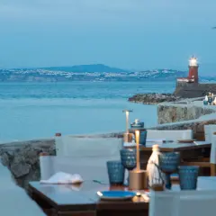 Tavoli apparecchiati con vista sul mare e un faro rosso, un invito a cena a Ischia.