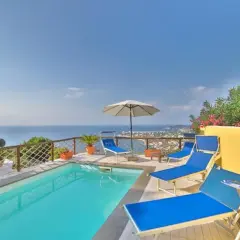 Piscina con lettini blu e vista mare a Ischia. Un angolo di paradiso, un dolce Poseidon che invita al relax.