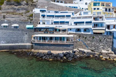 Hotel Celestino Ischia, con la sua architettura bianca e blu, si affaccia sul mare cristallino, incastonato nella roccia.