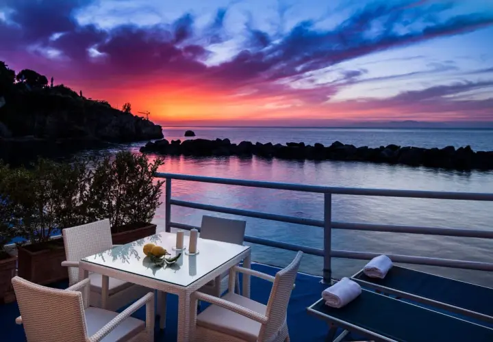 Terrazza con tavolo e sedie, lettini prendisole e un tramonto mozzafiato sul mare, un sogno in un blu resort Ischia.